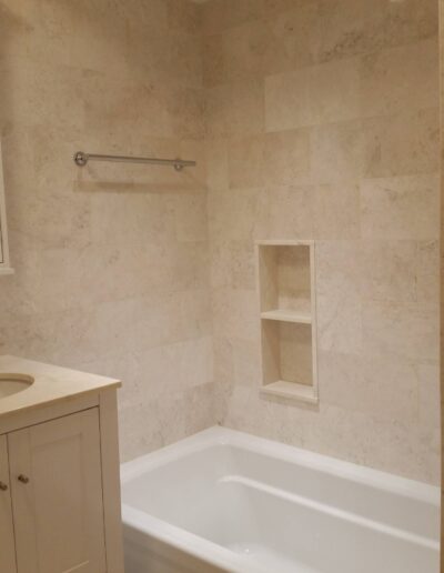 A modern bathroom with a white bathtub and marble walls featuring built-in shelves and a grab bar.