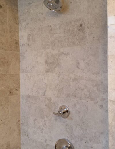 Modern shower with wall-mounted showerhead and controls on marble tile.