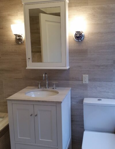 A modern bathroom featuring a vanity with a sink, a mirror above it, and wall sconces on either side, alongside a toilet to the right.