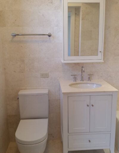 A modern bathroom with beige tiles featuring a white toilet, sink vanity, and a mirrored medicine cabinet.