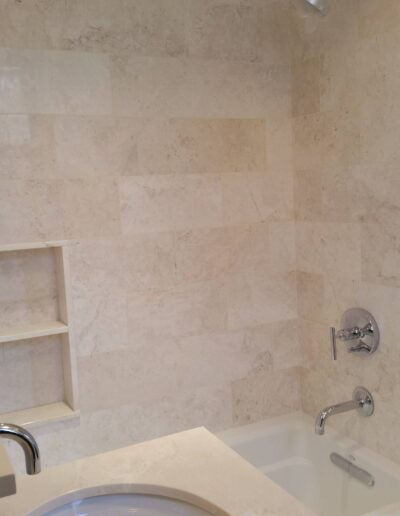 A modern bathroom corner with marble tiles, a built-in bathtub, and nickel-finished fixtures.