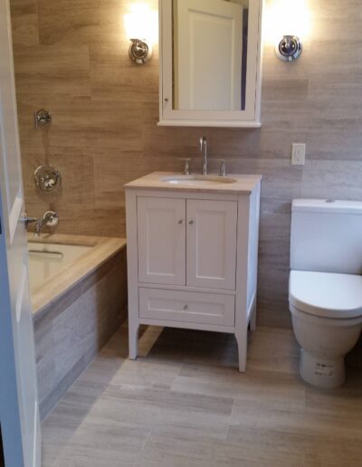 Modern bathroom with a beige tile design featuring a vanity, mirror, bathtub, and toilet.