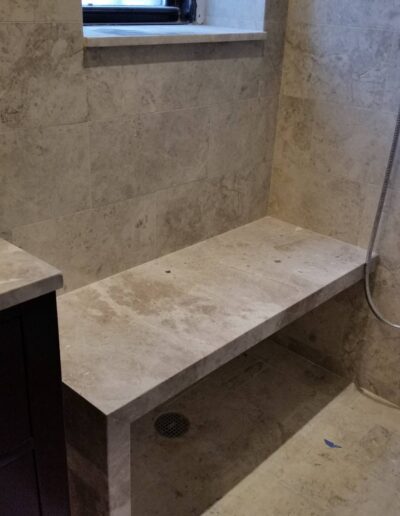 A modern bathroom under construction featuring a stone shower bench and tiled walls with a window.