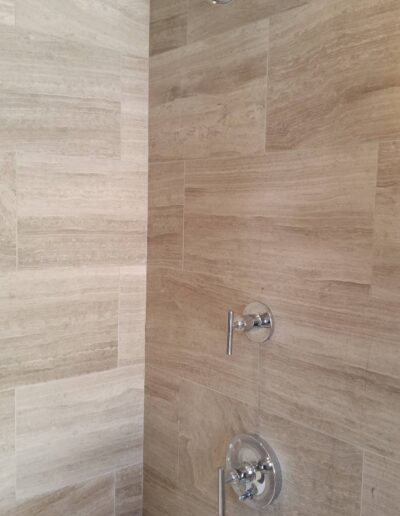 Contemporary bathroom shower with beige tile wall and stainless steel fixtures.