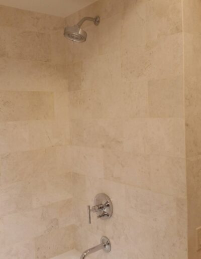 A light-colored tiled bathroom wall with a showerhead above a bathtub.