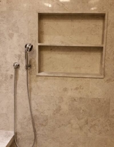 A shower head on the left with a built-in shelf on the right, against a tiled wall.