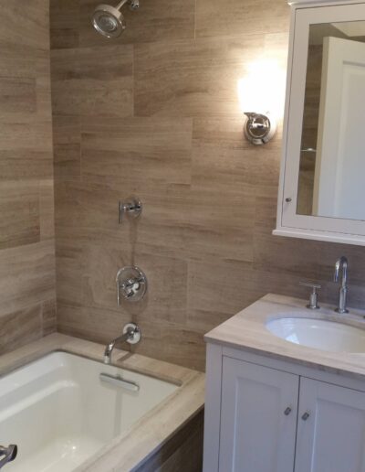 Modern bathroom interior with a built-in bathtub, tiled walls, and a vanity with sink and mirror.