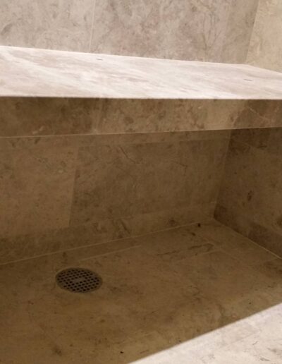 Modern beige tiled walk-in shower with built-in bench and glass door.