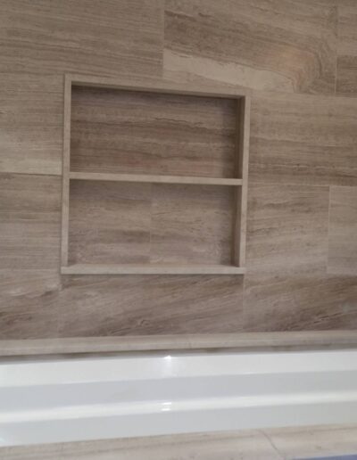 A modern bathroom with a built-in bathtub and beige tile walls featuring a recessed niche for bathroom items.