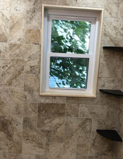 A tiled shower with a window overlooking greenery and multiple shelves.