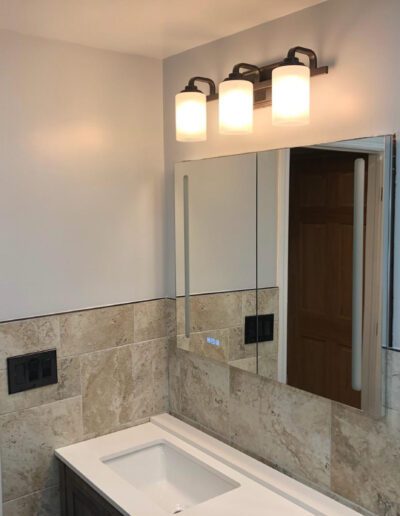 A modern bathroom with a well-lit vanity mirror and a tiled backsplash.