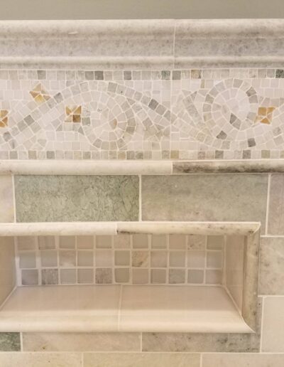 A built-in tiled niche in a shower with mosaic trim detailing.