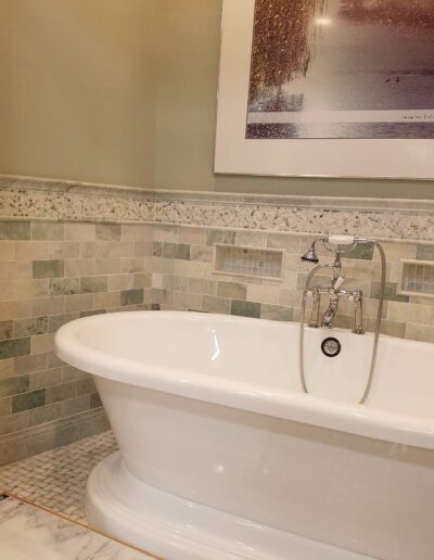 A modern freestanding bathtub with silver fixtures in a bathroom with tiled walls and flooring.