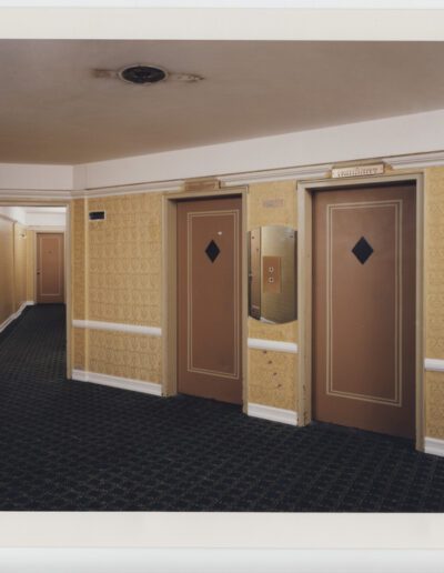 Hotel corridor with patterned wallpaper and two elevator doors.