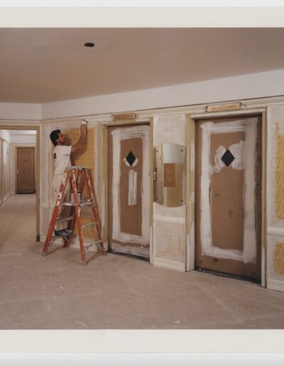 Two people applying wallpaper in a room with multiple doors.