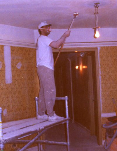 Man painting a ceiling while standing on scaffolding indoors.