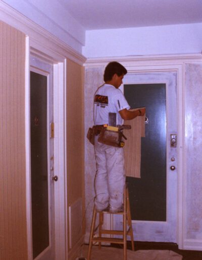 Man painting a wall while standing on a ladder.