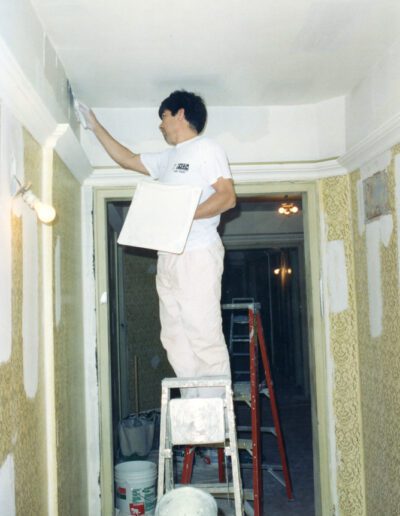 Man painting a wall while standing on a ladder in a hallway under renovation.