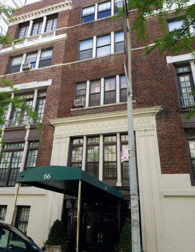 A multi-story brick building with an awning labeled "66" and several window air conditioning units.