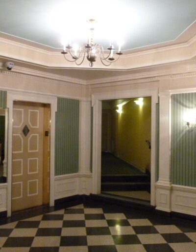 An elegant foyer with checkered flooring, pastel green walls, and classic lighting fixtures.