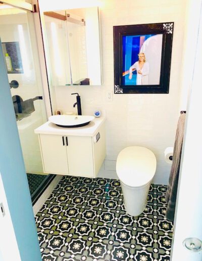 A modern bathroom with a patterned floor, a white sink, toilet, and a television screen embedded in the wall.