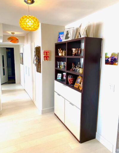 A modern hallway featuring a dark bookshelf with various decorative items, lit by a unique golden pendant light.