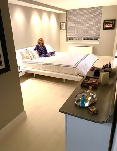 A person sitting on a bed in a well-lit, modern bedroom with a neat bedside area.