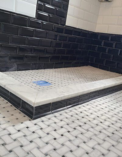 Modern bathroom with black subway tiles and white marble floor featuring a built-in shower area.