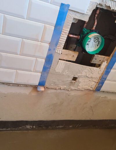 In-progress plumbing and tiling work with an exposed water valve and protective tape.