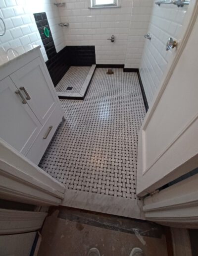 A bathroom under renovation with white subway tiles, a black and white tiled floor, and new fixtures partially installed.