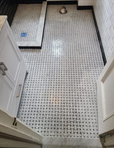 A bathroom under renovation with a herringbone tile floor and white subway-tiled walls, featuring a freestanding bathtub and protective covering on surfaces.