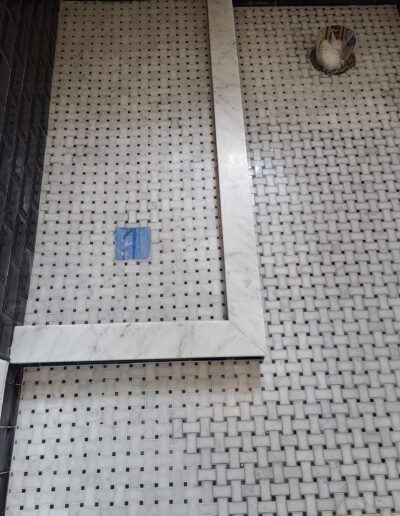 Tiled wall with a partial vertical marble trim, a small blue square tile, and a disconnected electrical outlet box.