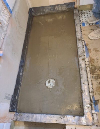 Renovation in progress: a shower pan under construction with wet mortar mix, surrounded by unfinished walls and flooring.