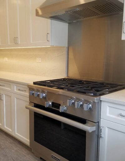 A modern kitchen interior with stainless steel stove, white cabinets, and marble countertops.