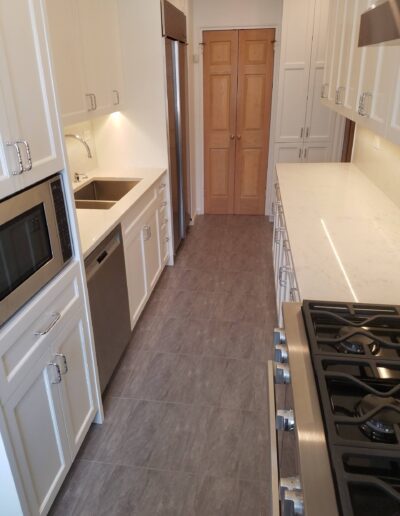 A modern kitchen with white cabinetry, stainless steel appliances, and gray floor tiles.