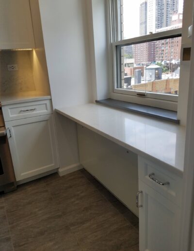 Modern kitchen with white cabinets, stainless steel appliances, and a window overlooking the city.