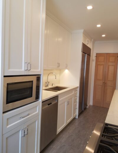 A modern kitchen with white cabinets, stainless steel appliances, and a light countertop.