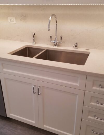 A modern kitchen with stainless steel sink, white cabinets, and a dishwasher.