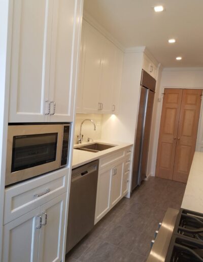 A modern kitchen interior with white cabinetry and stainless steel appliances.