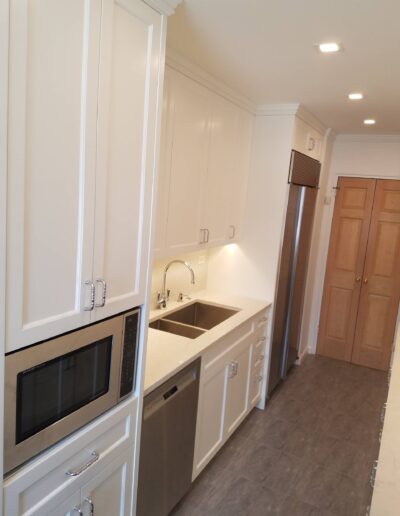 A modern kitchen interior with white cabinetry, stainless steel appliances, and grey flooring.