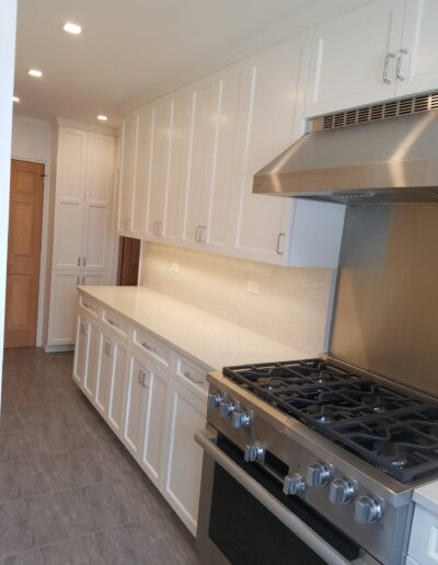 A modern kitchen interior featuring stainless steel appliances, white cabinetry, and a stone countertop.