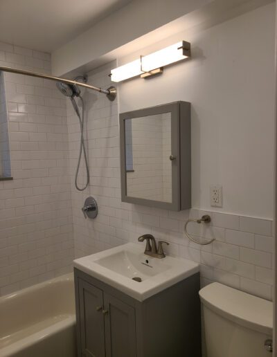 A modern bathroom featuring a white subway-tiled shower, a gray vanity with a sink, and a mirrored medicine cabinet.