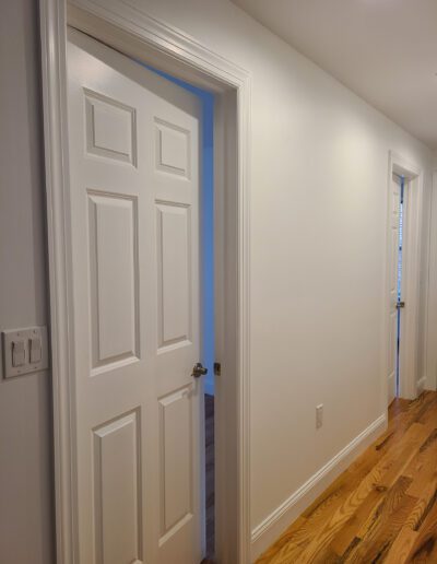 An open white door leading to a room with blue walls, viewed from a hallway with wooden flooring.