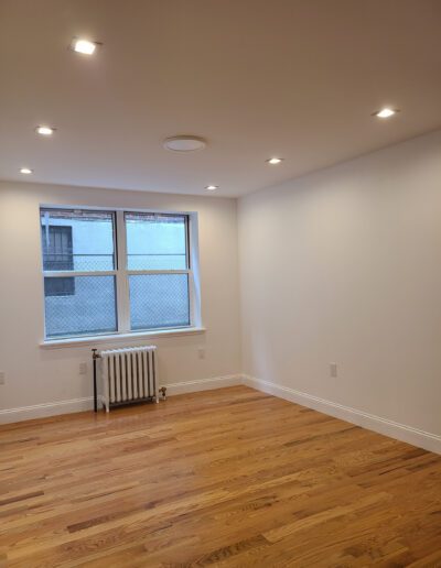 Empty room with hardwood floors, recessed lighting, a radiator under a window, and white walls.