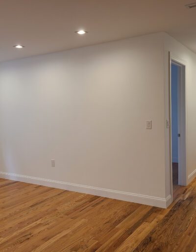 Modern empty room with hardwood floors and a closed door, with a glimpse of a tiled bathroom area to the right.