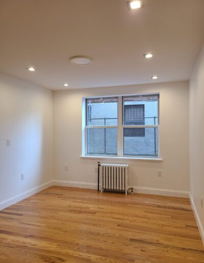 Empty room with hardwood flooring, a radiator under a window with a street view, and recessed lighting.