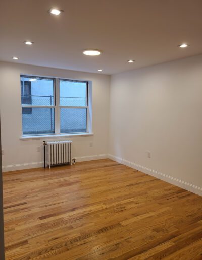 An empty room with hardwood floors, white walls, and two windows letting in natural light.