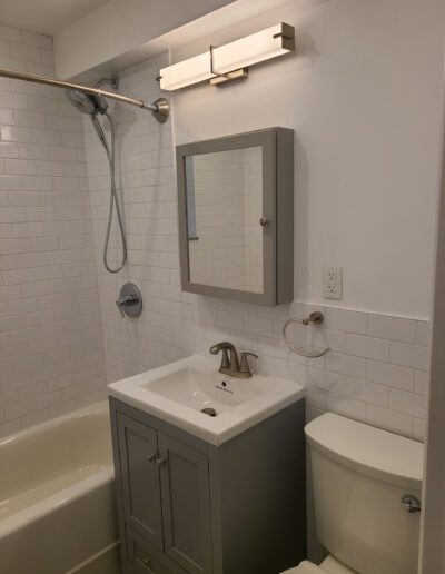 A modern bathroom interior with white subway tiles, featuring a shower, sink with vanity, toilet, and wall-mounted mirror.