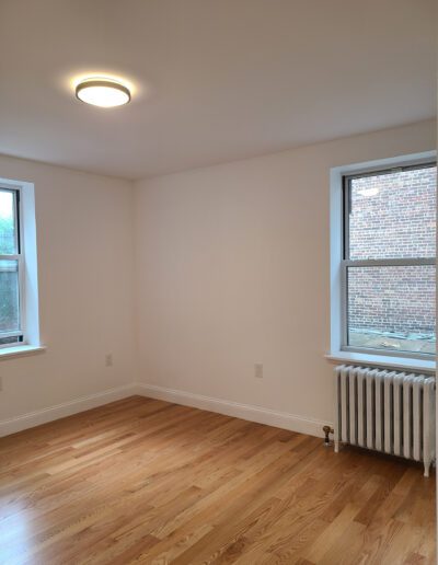 Empty room with hardwood floors, a radiator, and two windows.