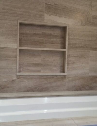 Modern bathtub with beige tile surround and built-in shelf.